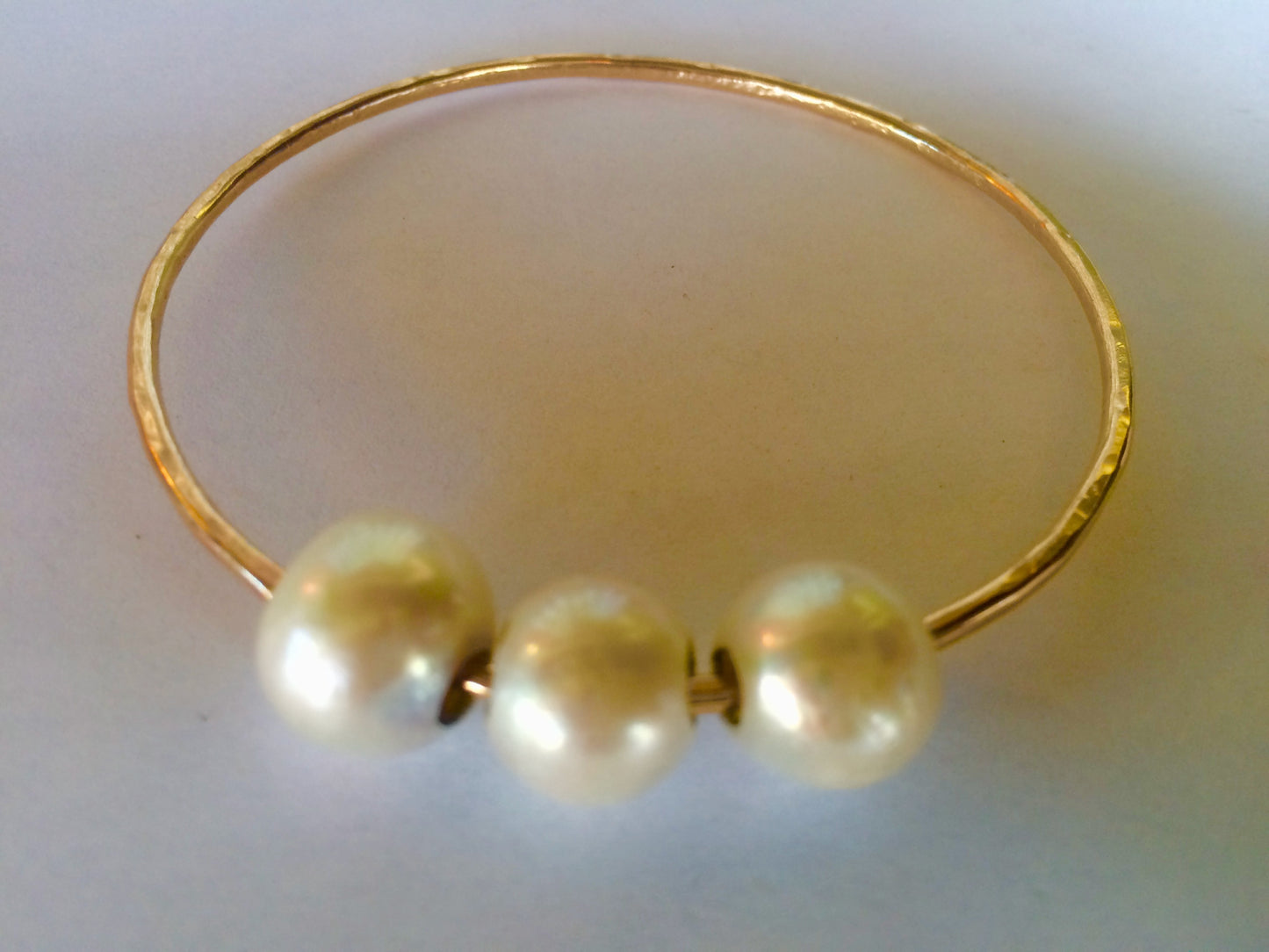 Close-up of the Triple Lux gold-filled bangle bracelet highlighting three luminous white Edison pearls on a soft neutral background.