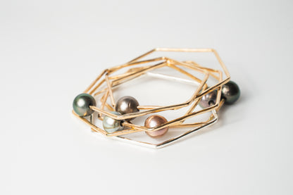 Stacked Lōkahi gold-filled geometric bangles featuring mixed-tone Tahitian pearls in green, silver, and blush hues on a white background.
