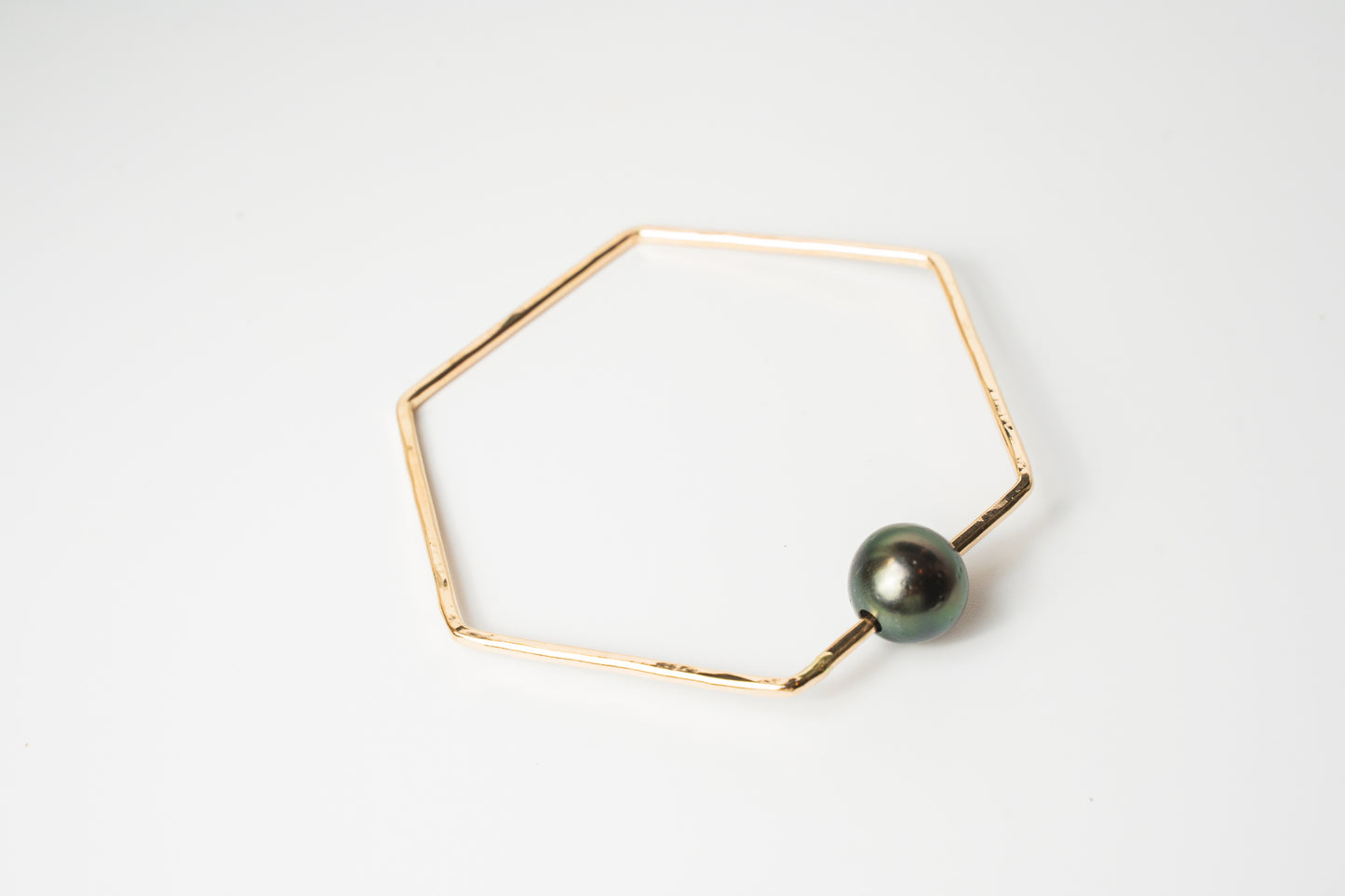 The Lōkahi gold-filled geometric bangle bracelet featuring a single dark black Tahitian pearl on a white background.