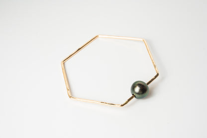 The Lōkahi gold-filled geometric bangle bracelet featuring a single dark black Tahitian pearl on a white background.