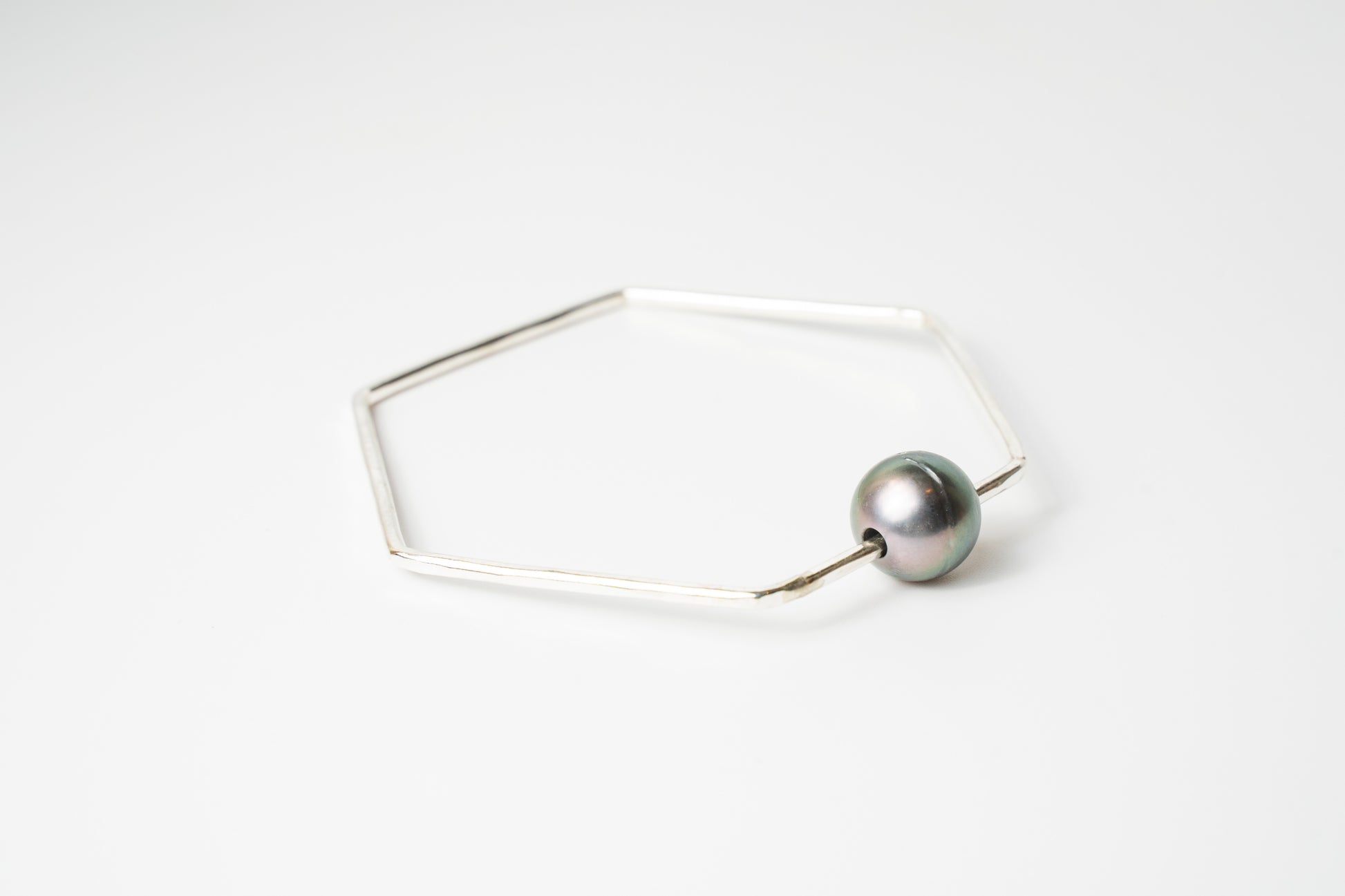 Angled view of The Lōkahi silver geometric bangle bracelet featuring a single silver Tahitian pearl on a white background.