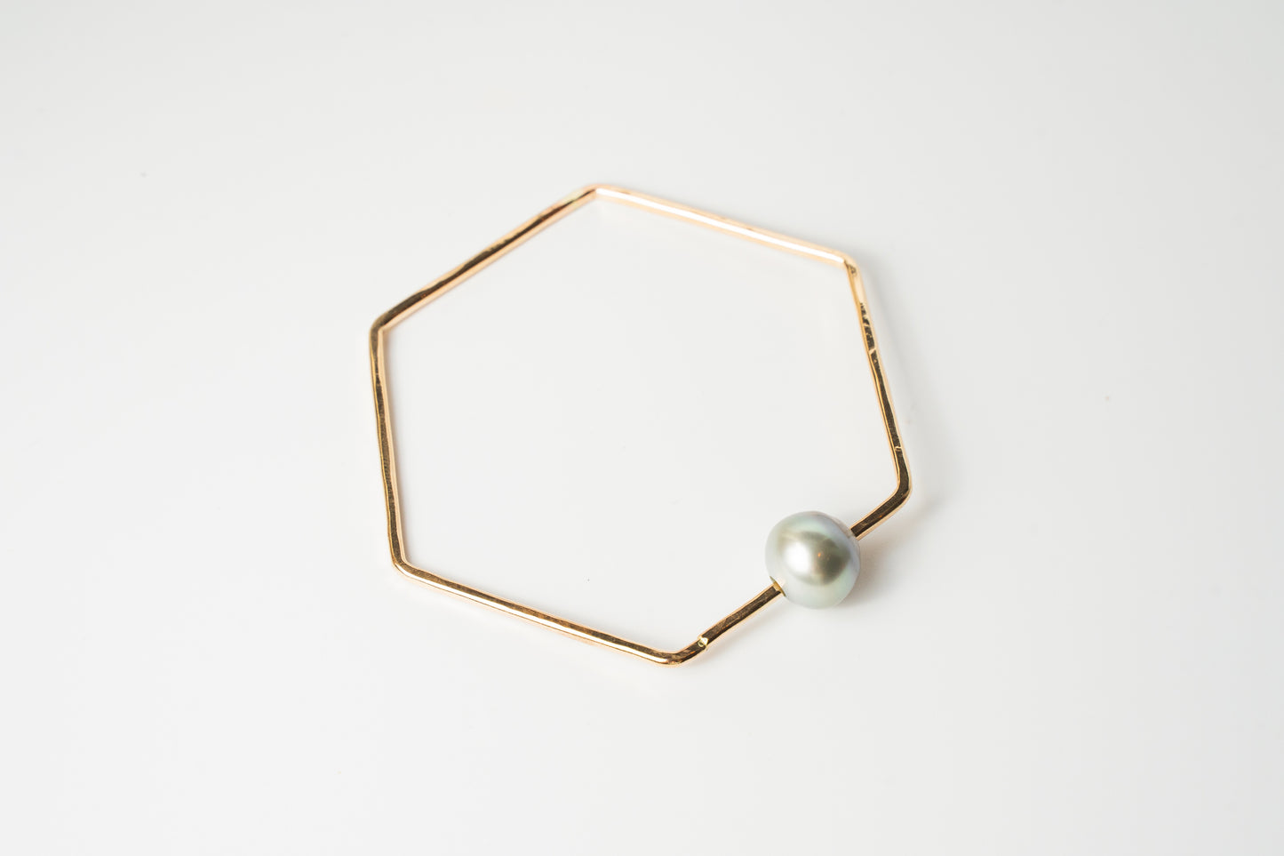 Front view of The Lōkahi gold-filled geometric bangle bracelet featuring a single light-toned or white Edison pearl on a white background.
