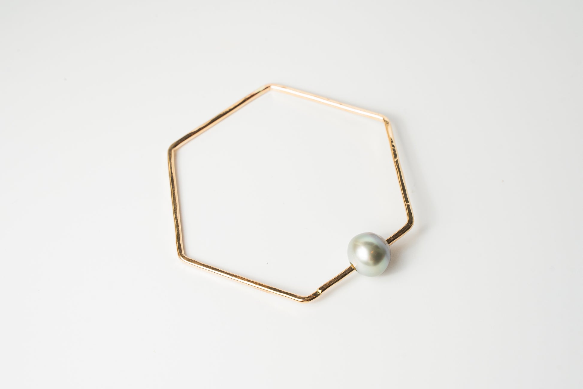 Front view of The Lōkahi gold-filled geometric bangle bracelet featuring a single light-toned or white Edison pearl on a white background.