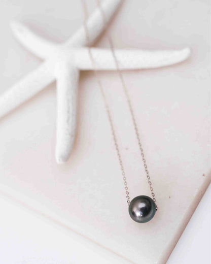 The Mo‘i Necklace with a single Black Tahitian pearl on a fine silver chain, styled on a white starfish background.