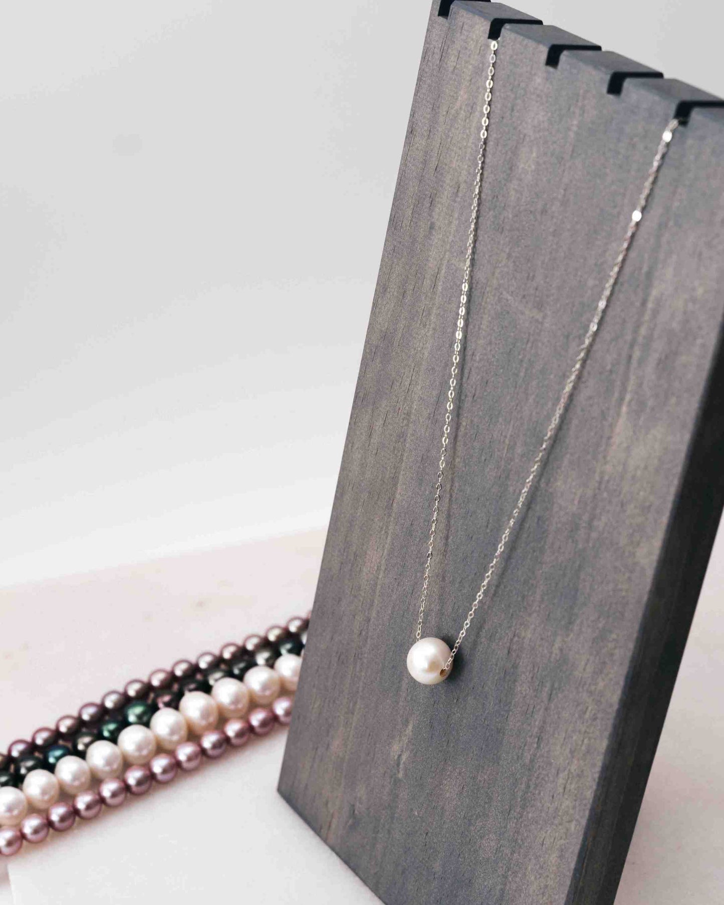 White Edison pearl necklace on a delicate silver chain displayed on a wooden jewelry stand.