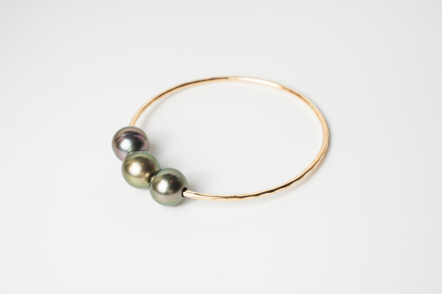 Triple Lux gold-filled bangle bracelet featuring three Tahitian pearls in soft green and iridescent tones on a white background.