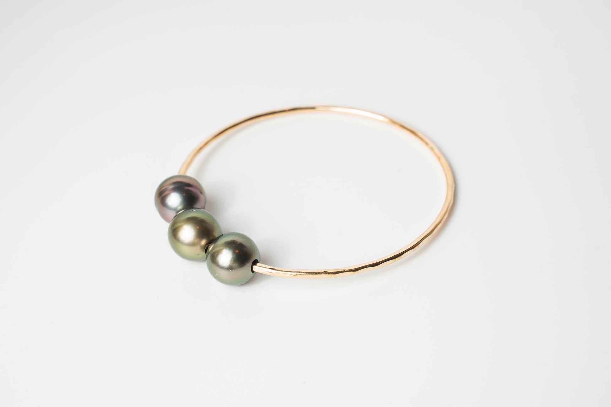Triple Lux gold-filled bangle bracelet featuring three Tahitian pearls in soft green and iridescent tones on a white background.