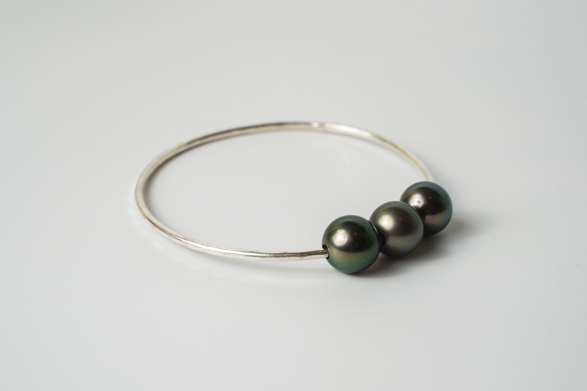 Side view of the Triple Lux gold-filled bangle bracelet with three Tahitian pearls in deep black and iridescent tones on a white background.
