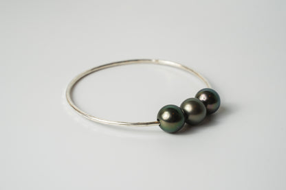 Side view of the Triple Lux gold-filled bangle bracelet with three Tahitian pearls in deep black and iridescent tones on a white background.