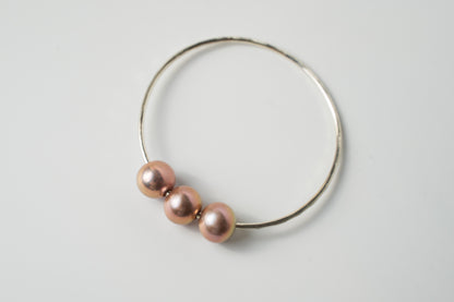 Angled view of the Triple Lux silver bangle bracelet with three blush-toned or pink Edison pearls on a white background.