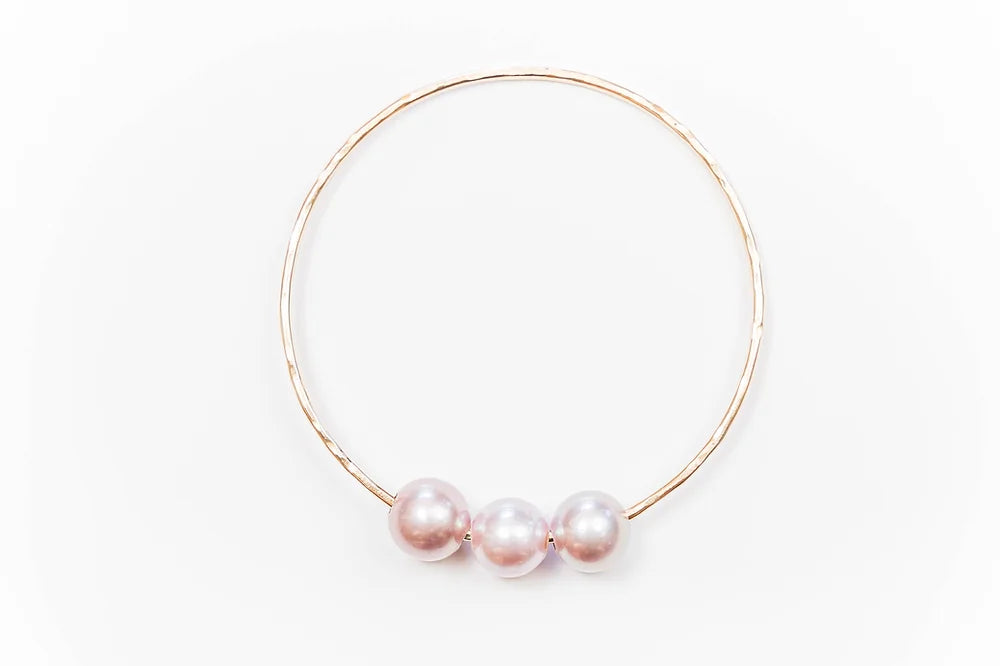 Top view of the Triple Lux gold-filled bangle bracelet with three soft blush or pink Edison pearls centered along the band on a white background.